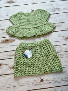 two green crocheted outfits sitting on top of a wooden floor next to each other