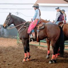 two women in cowboy hats are riding horses on a dirt ground with other people behind them