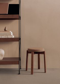 a wooden shelf with books and a white vase sitting on the floor next to it