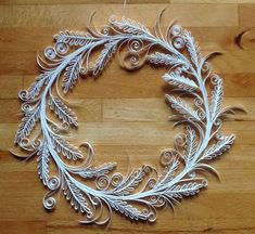 a white paper wreath on top of a wooden floor with leaves and swirls around it