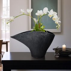 a black vase with white flowers in it on a table next to a lit candle