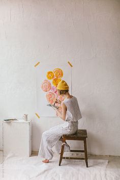 a woman sitting on a stool in front of a piece of art that is hanging on the wall