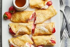 pastries with strawberries and powdered sugar on a white plate next to silverware