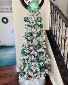 a christmas tree decorated with green and white ornaments in front of a clock on the wall