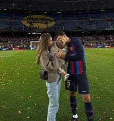 a man and woman holding a baby in front of a soccer field