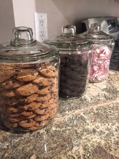 three glass jars filled with cookies on top of a counter