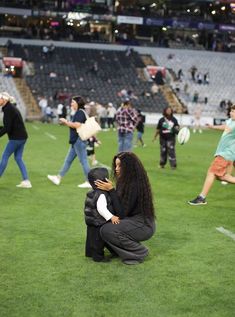 a woman kneeling down next to a child on top of a lush green soccer field