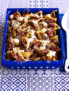 a blue casserole dish with meat and cheese on it next to a white utensil