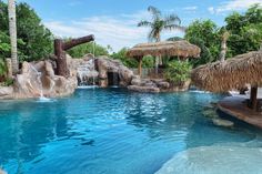 an outdoor swimming pool with waterfall and tiki huts on the sides, surrounded by palm trees