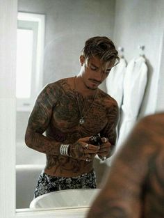 a man with tattoos is looking at his cell phone in the bathroom while standing next to a sink