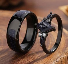 two black rings with diamonds on them sitting on top of a wooden table next to each other