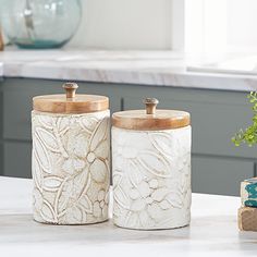 two white canisters sitting on top of a counter next to a potted plant