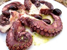 an octopus is cut in half on a white plate with olives and parmesan cheese