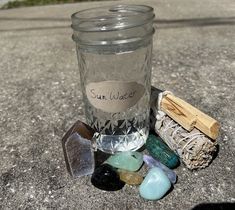 a glass jar filled with lots of different colored rocks next to a small wooden stick