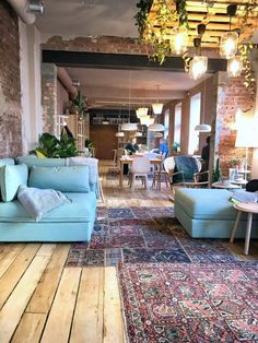 a living room filled with furniture and lots of plants hanging from the ceiling next to a brick wall