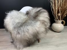 a furry animal is standing next to a vase with dry grass in it's mouth