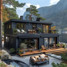 a black house sitting on top of a lush green hillside next to a body of water