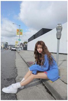 a young woman sitting on the side of a road next to a parking meter with her legs crossed