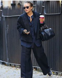 the woman is walking down the street with her hand in her pocket and holding a coffee cup