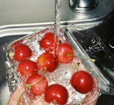 a person is washing cherries in a sink with ice and water pouring from a faucet