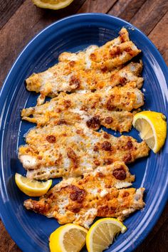 a blue plate topped with chicken covered in cheese and lemon slices