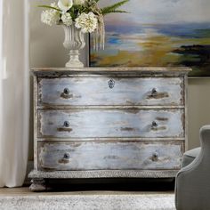 an old dresser with white flowers in a vase next to a painting on the wall