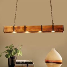 a wooden light fixture hanging over a table next to a potted plant and books