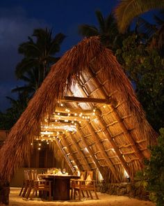 a tiki hut at night with lights on the roof and tables set up outside