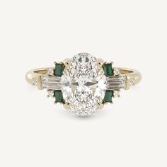 an oval diamond and emerald engagement ring with two baguettes on the side, set in yellow gold