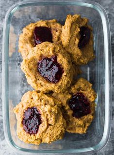 three cookies with jam in the middle are on a glass dish and one is cut in half