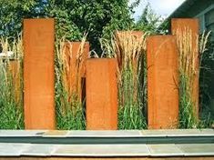 an outdoor garden with tall grass growing between two concrete pillars and a stone bench in front of it