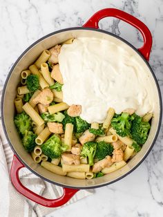 a red pot filled with pasta and broccoli covered in sauce on top of a marble counter