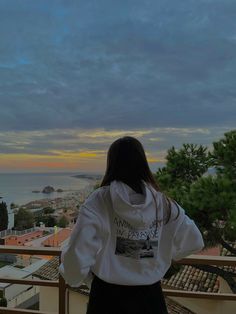 a woman standing on top of a balcony looking out at the ocean and buildings in the distance