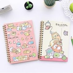 two notebooks with cartoon characters on them next to succulent plants and cacti