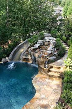 an outdoor swimming pool with waterfall and rock steps leading up to the water feature, surrounded by lush greenery