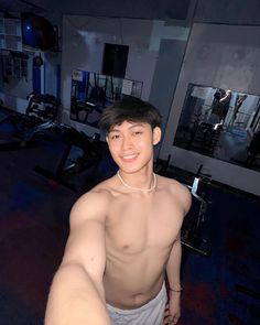 a shirtless young man is posing for the camera in a gym room with no shirt on