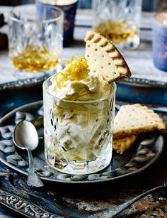 a glass with some food in it on a plate next to crackers and spoons