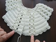 someone is crocheting a white sweater on a table