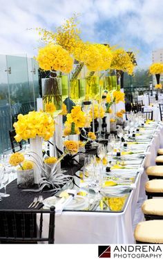 a long table is set with yellow flowers and vases on it for an event