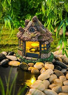 a small house made out of rocks next to a pond with water and plants around it