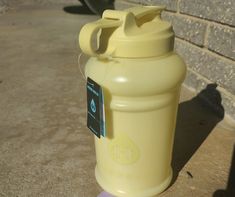 a yellow plastic water bottle sitting on the ground next to a brick wall and sidewalk