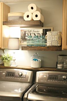 a washer and dryer in a small room with wooden shelves above the washers