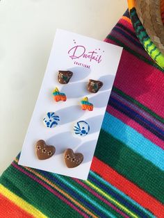 "Looking for cute Latino-inspired polymer clay earrings? Grab this four-pack of mini studs that scream \"Soy Latina!\" Handmade here in the Alamo City, these Mexican-style stud earrings are perfect for a fiesta! You get all four flatback earring sets! This set includes glazed barro pottery jarritos, colorful fiesta piñatas, glazed cazuelita barro pottery heart studs, and classic talavera patterned round studs. Lightweight and colorful, these earrings are petite (see measurements) making them great for those looking for adorable interchangeable pairs or those with multiple piercings. They are also great for giving as a gift or sharing with a friend! Each set is secured to steel silver-toned posts with UV resin, making them long-lasting. All earrings are made of quality FIMO brand polymer cl Mexican Clay Earrings, Frida Kahlo Party Decoration, Mexican Party Favors, Talavera Pattern, Unique Hair Bows, Pottery Heart, Charm Bar, Diy Gifts To Sell, Resin Making