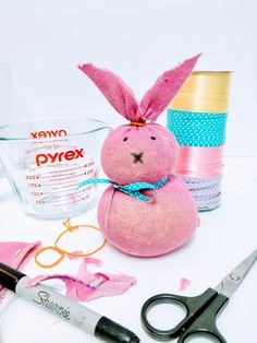 a pink bunny stuffed animal sitting next to scissors and other crafting supplies on a table