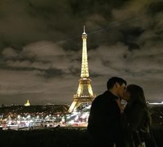 a man and woman standing in front of the eiffel tower at night, kissing