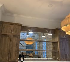 an empty kitchen with wine bottles on the counter and lights hanging from the ceiling above