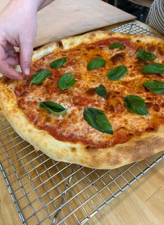 a pizza sitting on top of a metal rack covered in cheese and green leafy toppings