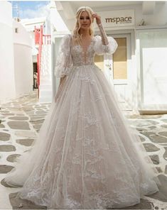 a woman in a white wedding dress standing on the street with her hands behind her head