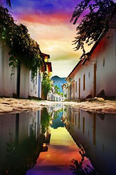 an alley way with water reflecting the buildings and trees on both sides, at sunset