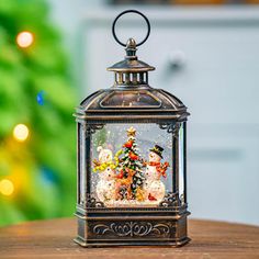 a small christmas tree in a glass container on top of a wooden table next to a green christmas tree